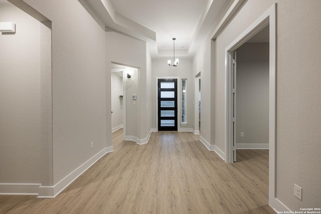 foyer entrance featuring a tray ceiling, light hardwood / wood-style floors, and an inviting chandelier