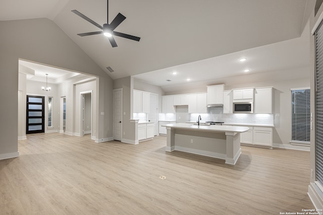 kitchen featuring sink, high vaulted ceiling, white cabinetry, stainless steel microwave, and an island with sink