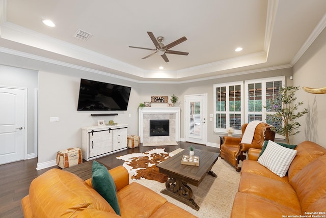 living room featuring dark wood-type flooring, crown molding, ceiling fan, a fireplace, and a tray ceiling