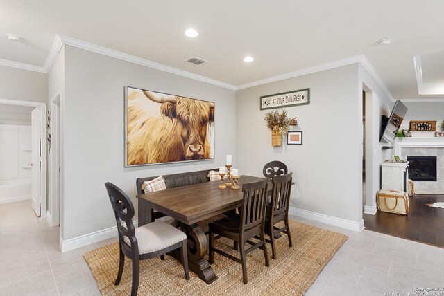 tiled dining room with ornamental molding and a tile fireplace