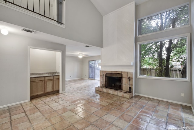 unfurnished living room with visible vents, baseboards, a tile fireplace, a high ceiling, and a ceiling fan