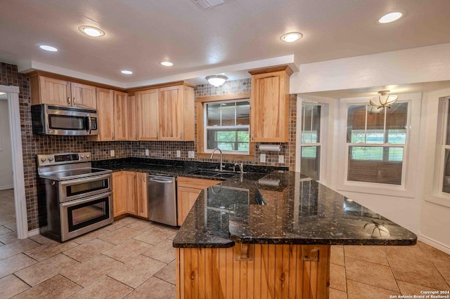 kitchen with stainless steel appliances, kitchen peninsula, sink, and dark stone countertops