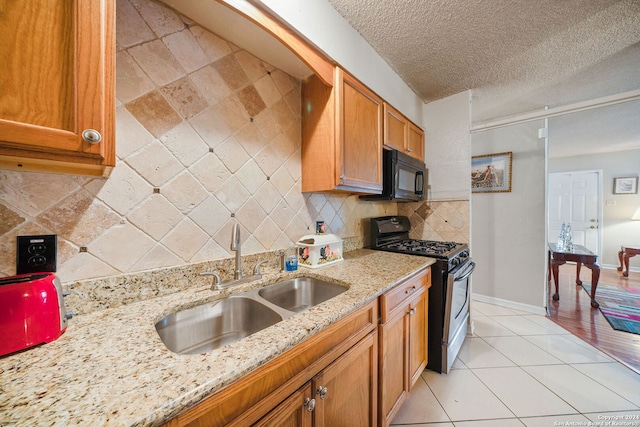 kitchen with light stone countertops, backsplash, a textured ceiling, sink, and black appliances