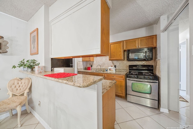 kitchen with light stone counters, kitchen peninsula, a textured ceiling, a breakfast bar area, and stainless steel range with gas stovetop