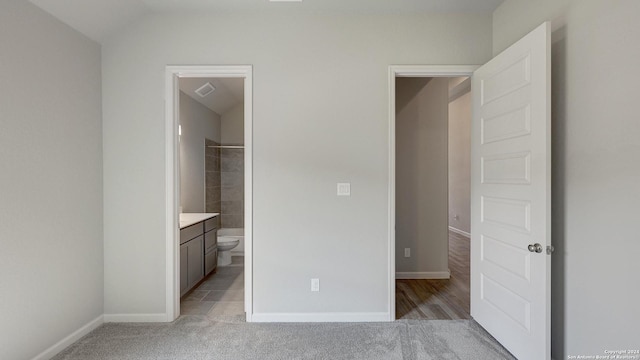 unfurnished bedroom featuring ensuite bathroom, vaulted ceiling, and light colored carpet