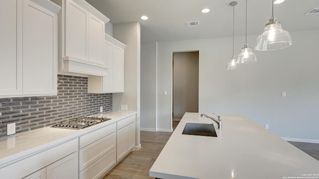 kitchen featuring sink, stainless steel gas cooktop, decorative light fixtures, white cabinets, and hardwood / wood-style flooring