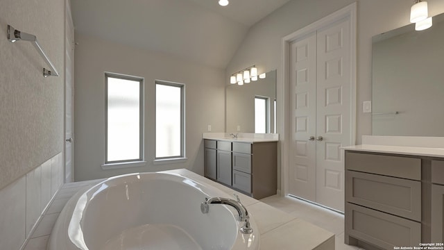 bathroom featuring a bathing tub, vanity, lofted ceiling, and tile patterned flooring