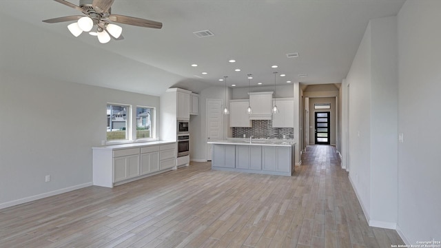 kitchen featuring decorative backsplash, appliances with stainless steel finishes, light wood-type flooring, a center island with sink, and white cabinetry