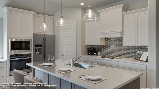 kitchen with appliances with stainless steel finishes, sink, a center island with sink, decorative light fixtures, and white cabinetry