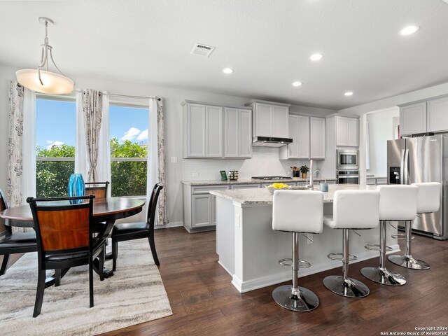 kitchen featuring a center island with sink, dark hardwood / wood-style flooring, stainless steel appliances, decorative light fixtures, and tasteful backsplash