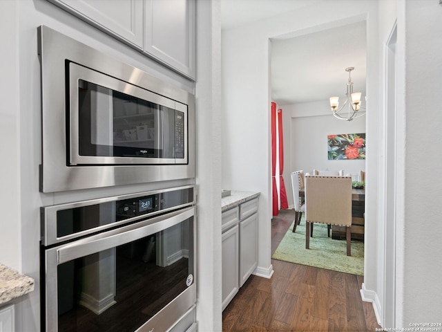 kitchen featuring white cabinets, light stone counters, a notable chandelier, dark wood-type flooring, and appliances with stainless steel finishes