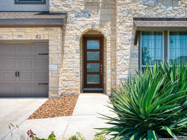 doorway to property featuring a garage, stone siding, and stucco siding