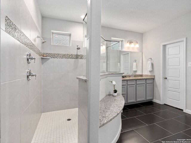 bathroom with tiled shower, tile flooring, and vanity