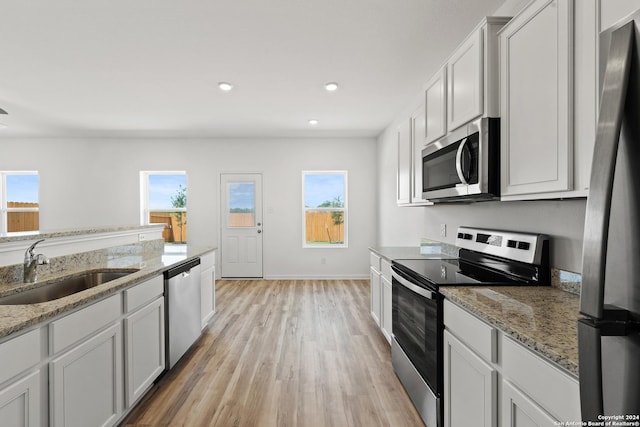 kitchen with stainless steel appliances, sink, white cabinets, and light stone counters