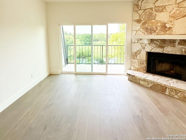 unfurnished living room featuring light wood-type flooring and a stone fireplace