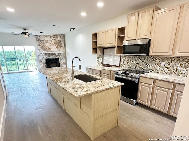 kitchen with light stone countertops, sink, stainless steel appliances, a center island with sink, and a stone fireplace