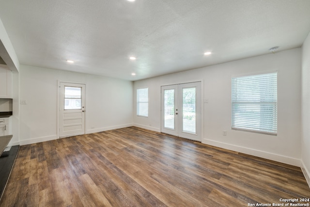 unfurnished living room with a textured ceiling, dark wood-type flooring, and french doors