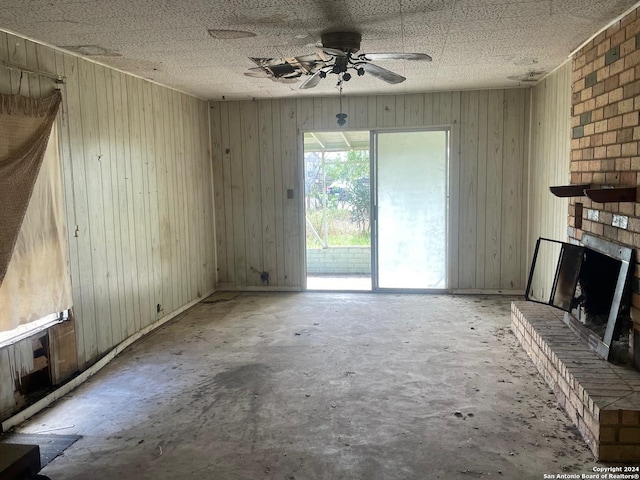 unfurnished living room with ceiling fan, wood walls, a fireplace, and unfinished concrete flooring