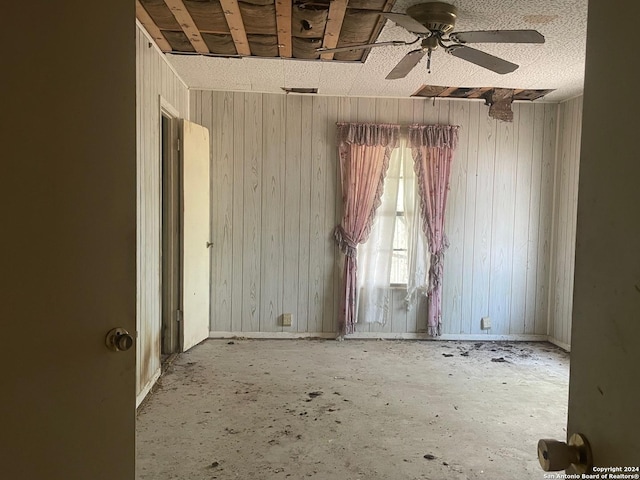 empty room featuring a ceiling fan and wooden walls