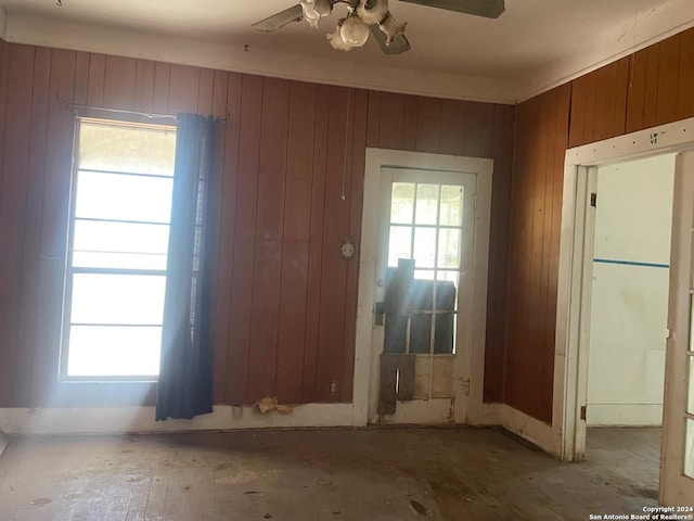 doorway featuring ceiling fan, wooden walls, and a healthy amount of sunlight