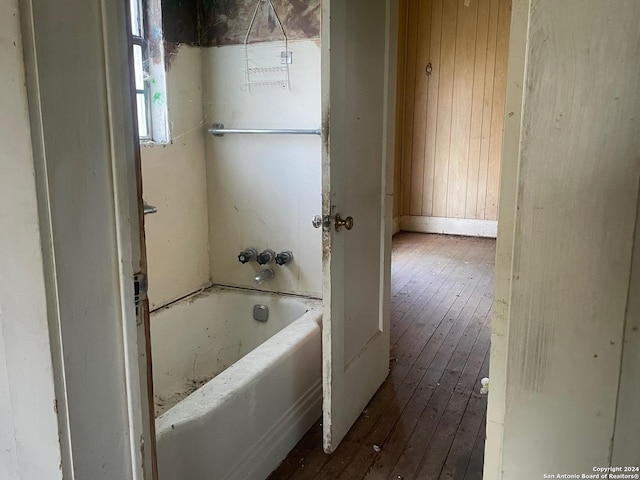 bathroom with a tub to relax in, wood walls, and wood finished floors