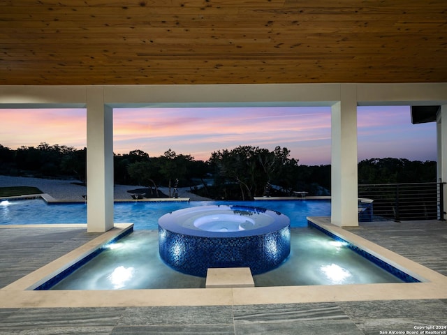 pool at dusk featuring an in ground hot tub and pool water feature