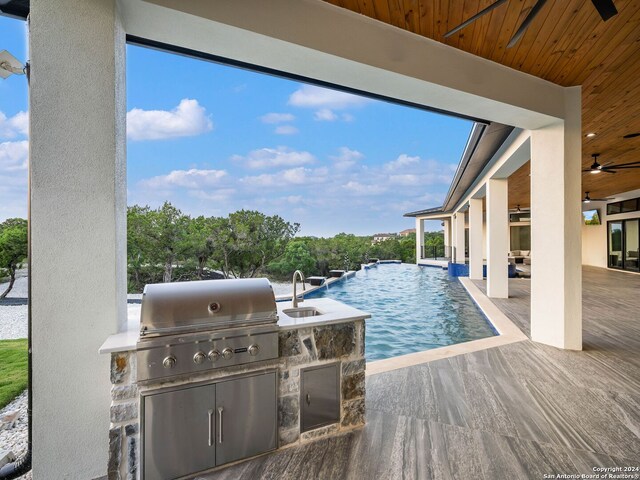 view of pool featuring pool water feature, an outdoor kitchen, area for grilling, a patio, and ceiling fan