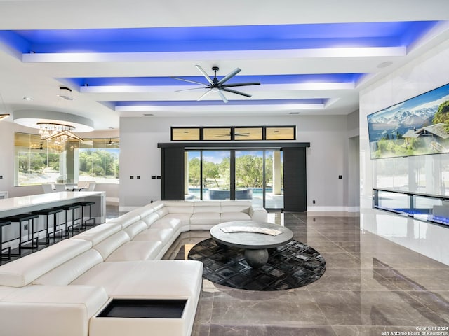 living room with ceiling fan with notable chandelier, tile patterned flooring, a tray ceiling, and a healthy amount of sunlight