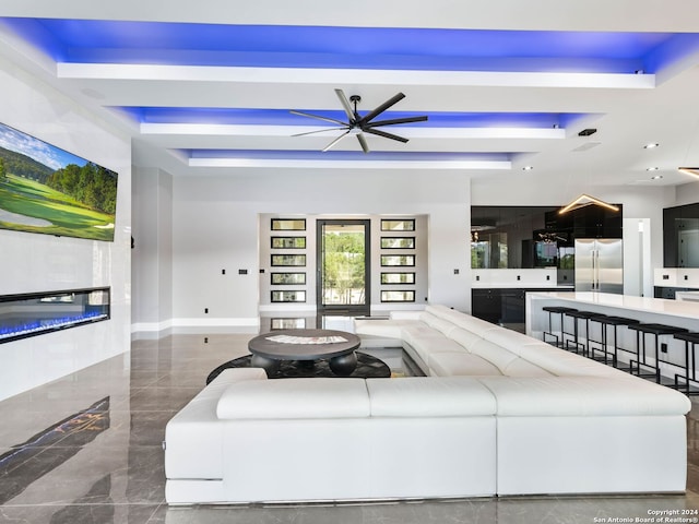 living room featuring a raised ceiling, ceiling fan, and dark tile patterned flooring