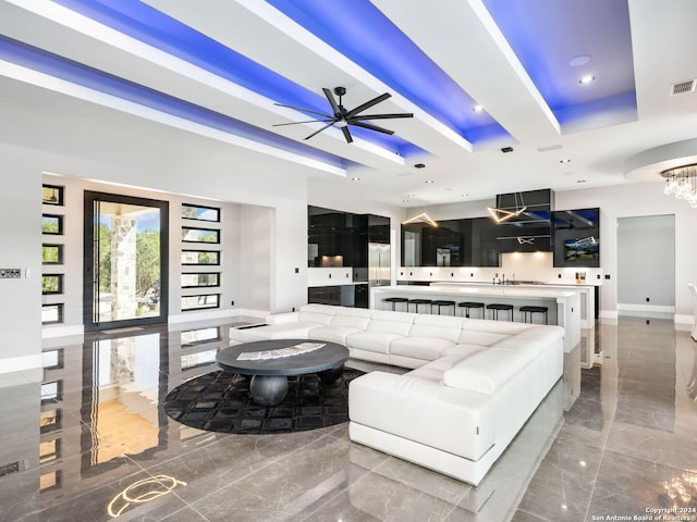 living room with ceiling fan with notable chandelier, tile patterned flooring, and a raised ceiling