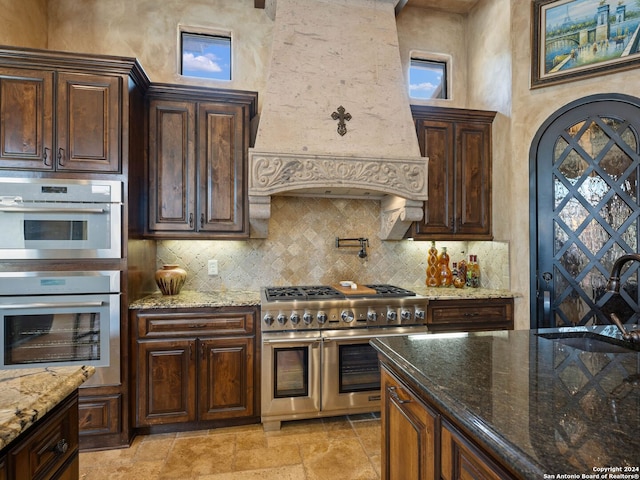 kitchen featuring light stone countertops, custom range hood, light tile floors, and appliances with stainless steel finishes