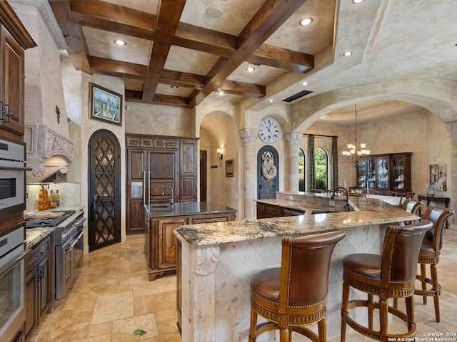 kitchen featuring dark stone countertops, appliances with stainless steel finishes, a large island, coffered ceiling, and light tile flooring