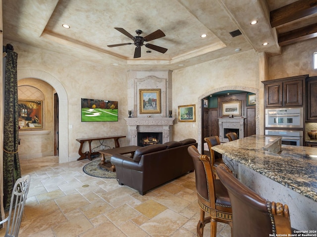 tiled living room with ceiling fan and a raised ceiling