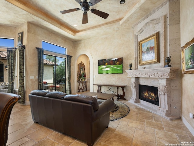 living room featuring a tray ceiling, a fireplace, ceiling fan, and tile floors