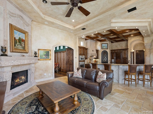 tiled living room featuring a fireplace, a towering ceiling, coffered ceiling, ceiling fan, and a raised ceiling