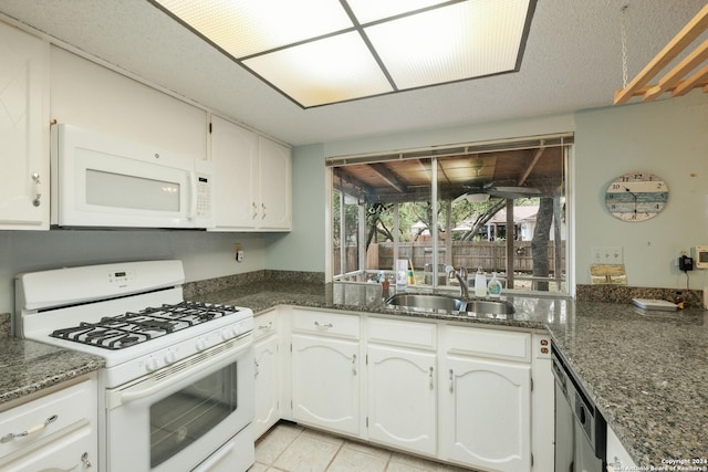 kitchen with white cabinetry, sink, dark stone counters, white appliances, and light tile patterned floors