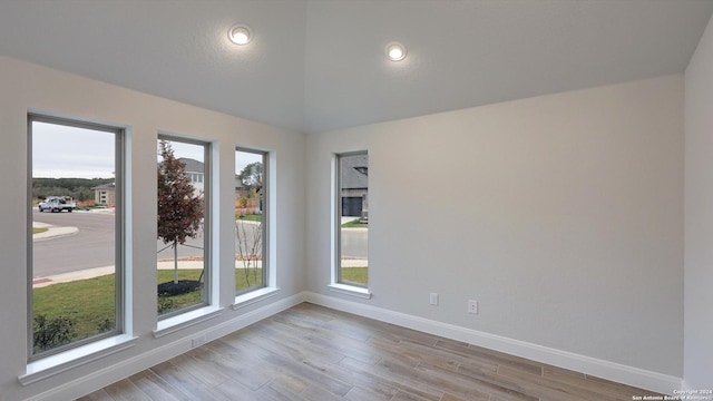 spare room with a healthy amount of sunlight, vaulted ceiling, and light hardwood / wood-style flooring