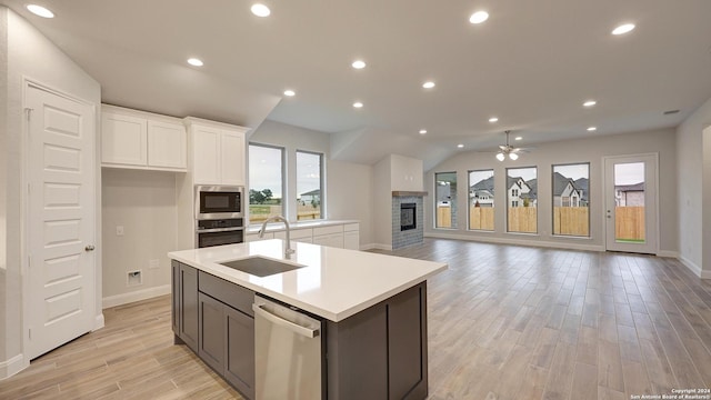 kitchen with stainless steel appliances, ceiling fan, sink, white cabinetry, and a stone fireplace