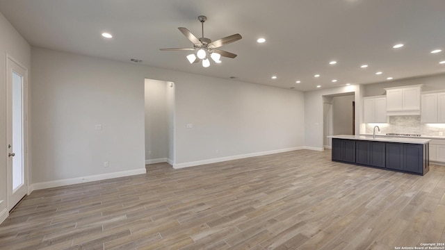 unfurnished living room with ceiling fan, light wood-type flooring, and sink