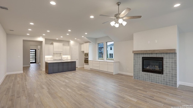 unfurnished living room with a tile fireplace, ceiling fan, and light hardwood / wood-style flooring