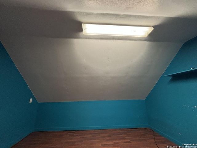 additional living space with hardwood / wood-style flooring, vaulted ceiling, and a textured ceiling