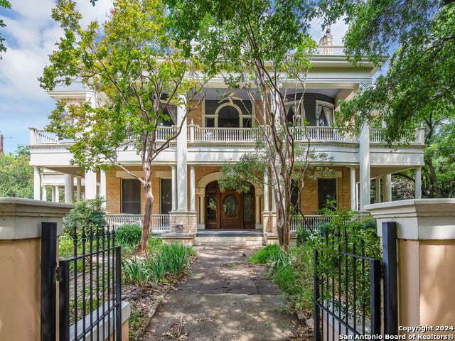 neoclassical / greek revival house featuring a porch, a gate, fence, and a balcony