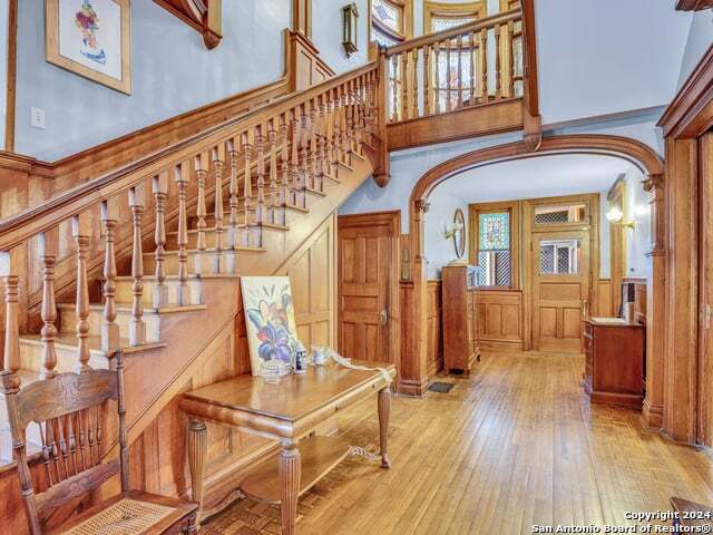 entrance foyer with light wood-type flooring, arched walkways, a towering ceiling, and stairs