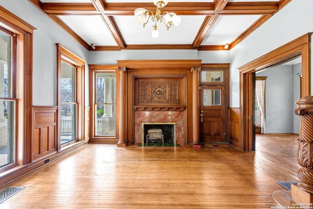 unfurnished living room featuring light wood-style flooring, a wainscoted wall, a premium fireplace, coffered ceiling, and visible vents