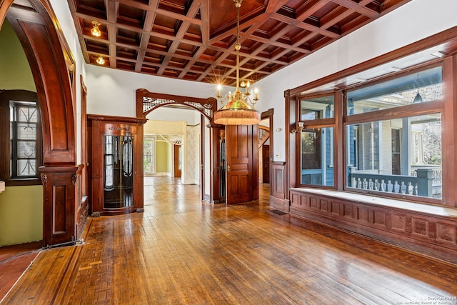 spare room with arched walkways, a notable chandelier, coffered ceiling, beam ceiling, and hardwood / wood-style floors