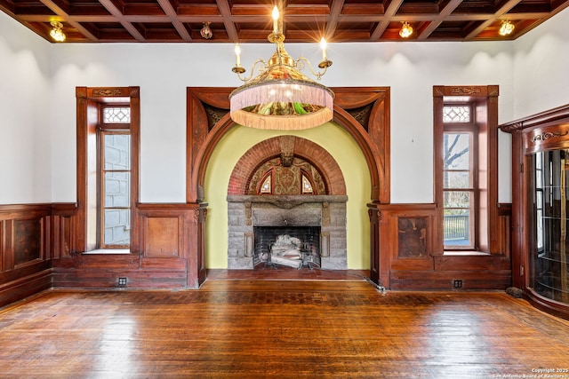 unfurnished living room featuring coffered ceiling, wainscoting, hardwood / wood-style floors, a fireplace, and a chandelier