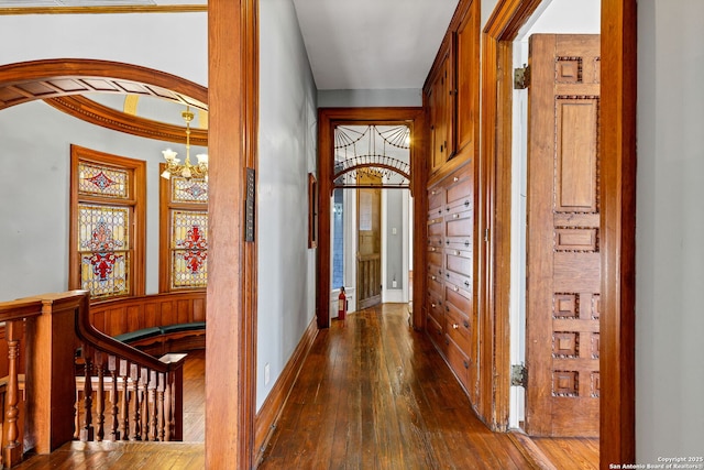 corridor featuring arched walkways, an inviting chandelier, dark wood-type flooring, an upstairs landing, and baseboards