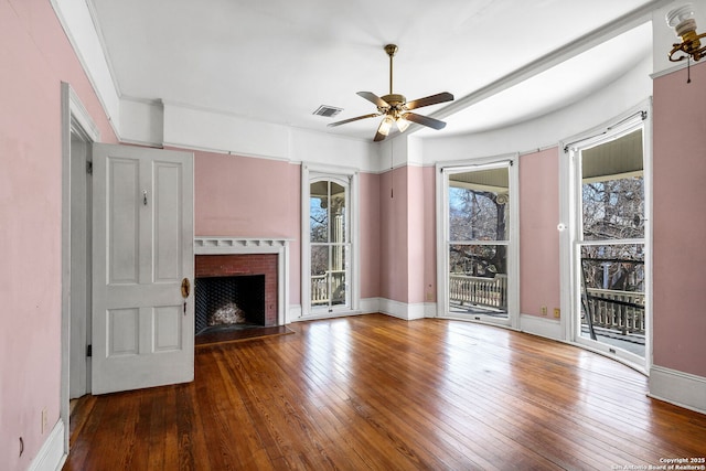 unfurnished living room with baseboards, visible vents, a ceiling fan, hardwood / wood-style flooring, and a brick fireplace