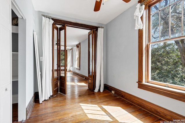 hall featuring light wood-style flooring, baseboards, and a wealth of natural light