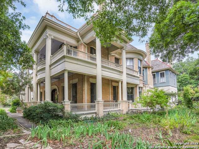 view of front of house featuring a balcony, covered porch, and brick siding